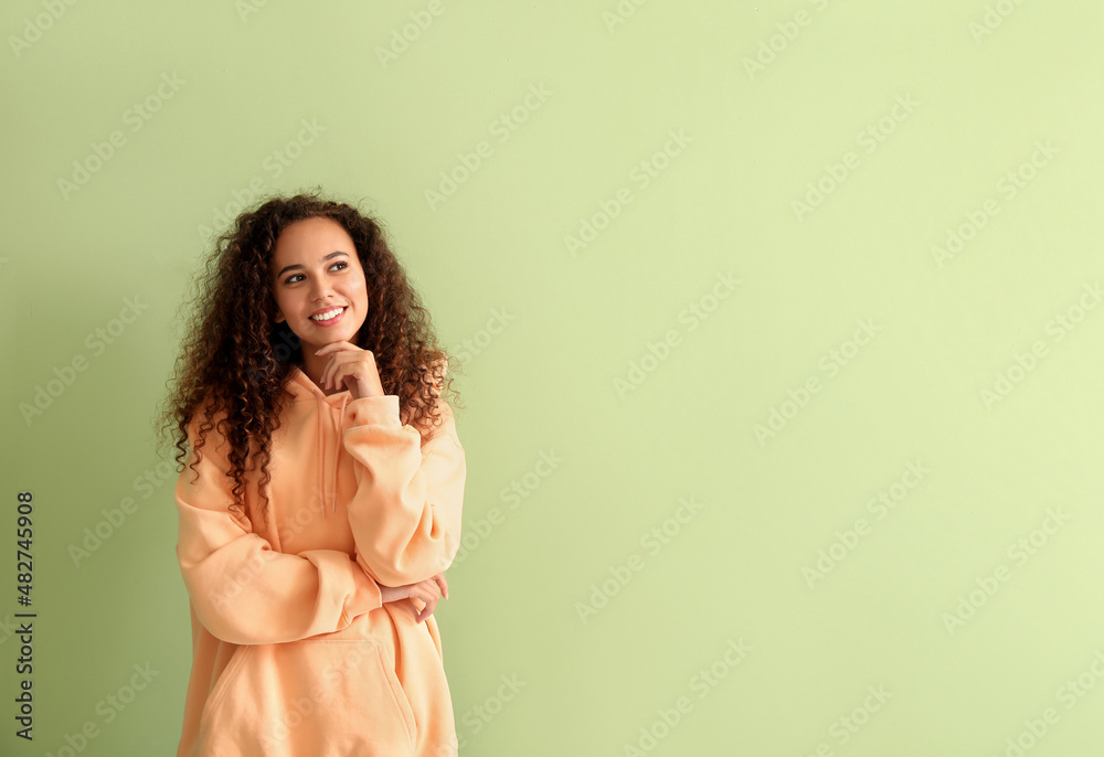 Beautiful young African-American woman in stylish hoodie on color background