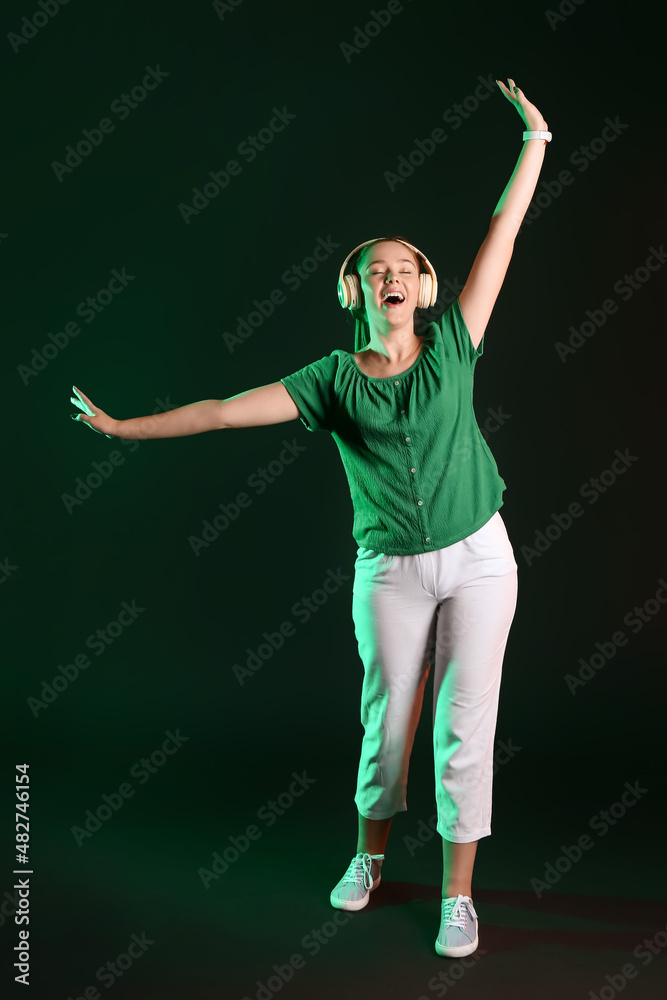 Cool young woman listening to music on dark background