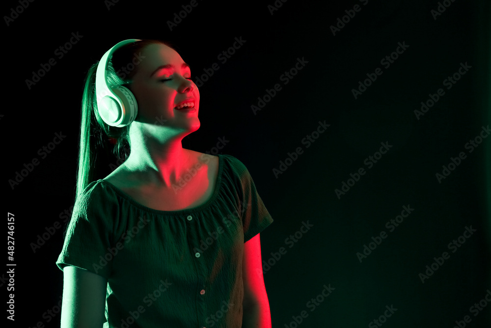 Cool young woman listening to music on dark background