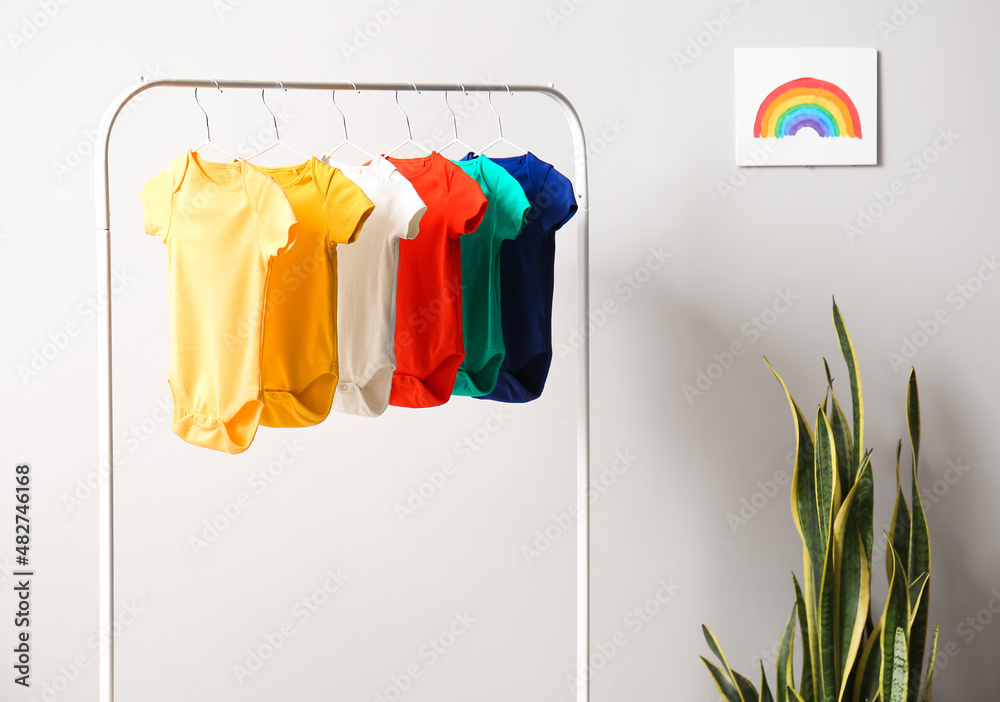 Rack with colorful baby bodysuits near light wall in room