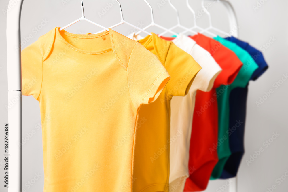 Rack with colorful baby bodysuits near light wall, closeup