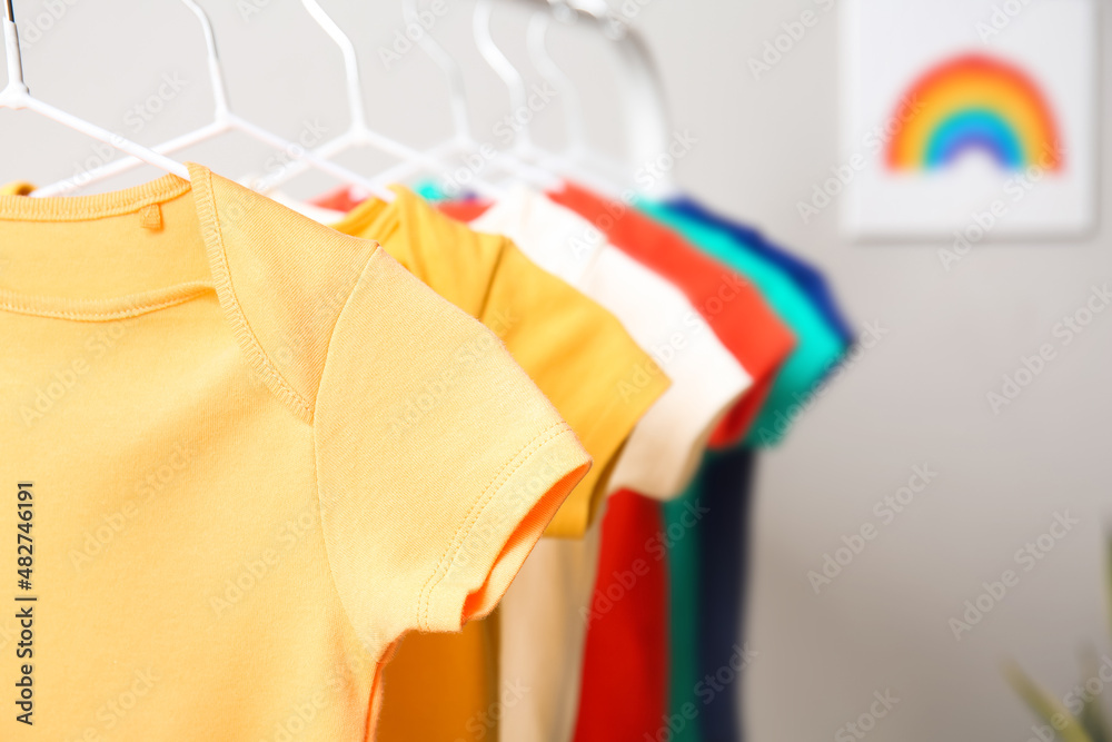 Rack with colorful baby bodysuits near light wall, closeup