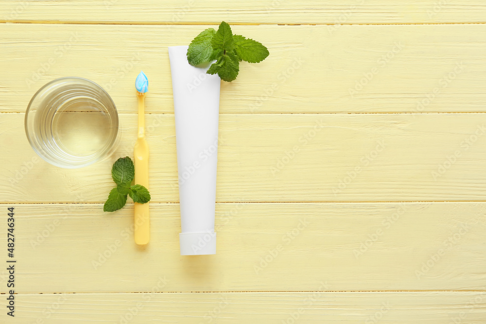 Tube with tooth paste, brush, mint and glass of water on color wooden background