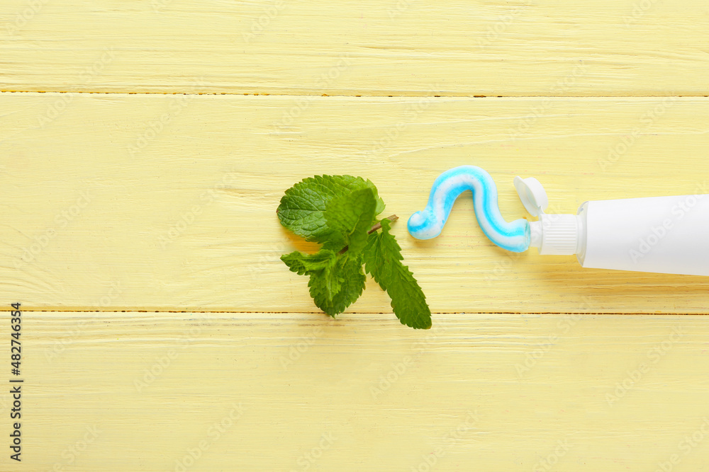 Tube with tooth paste and mint on color wooden background