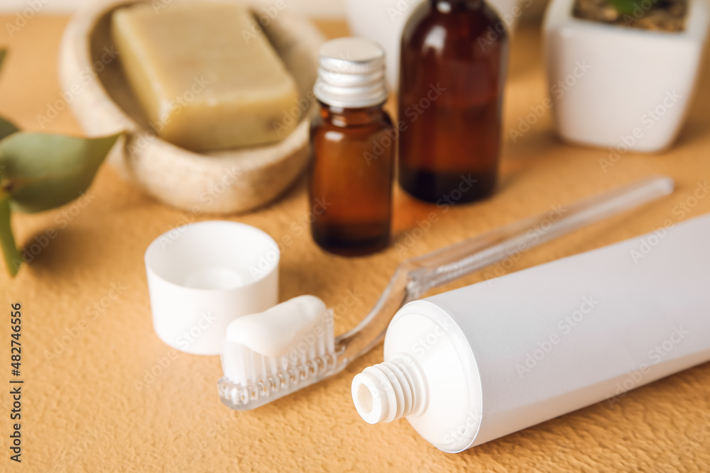 Opened tube with toothpaste, toothbrush and bath accessories on color table, closeup