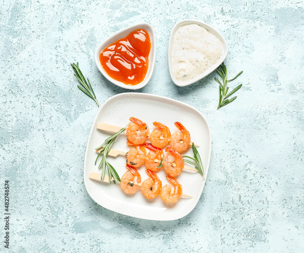 Plate with grilled shrimp skewers and sauces on blue background