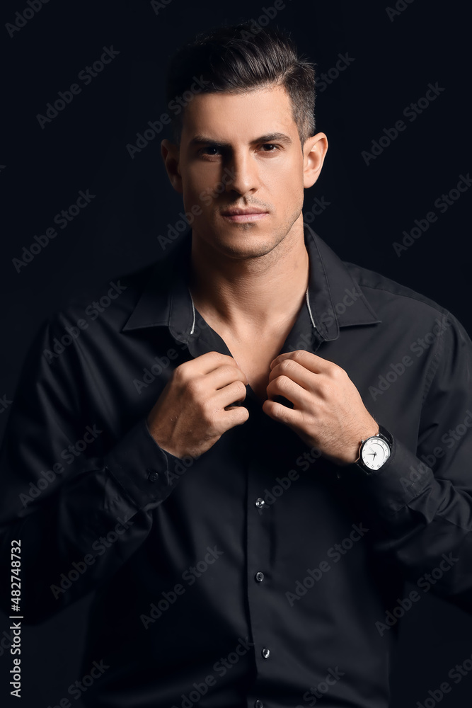 Fashionable gentleman adjusting shirt on dark background