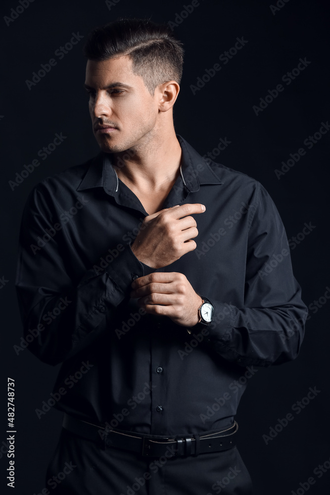 Fashionable gentleman adjusting sleeve and looking aside on dark background