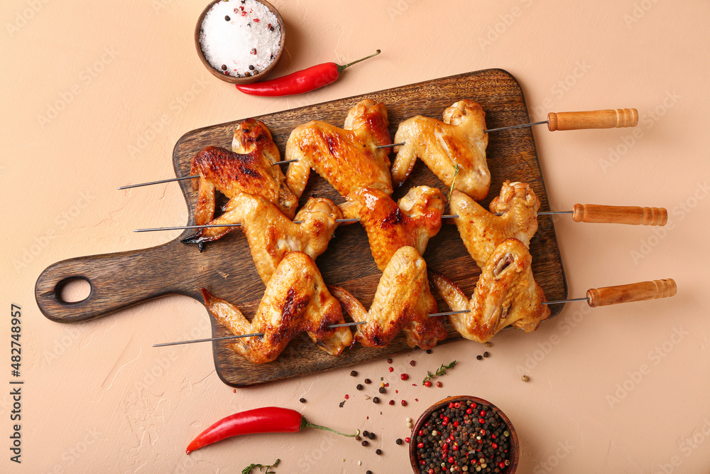 Wooden board with grilled chicken wings skewers on beige background