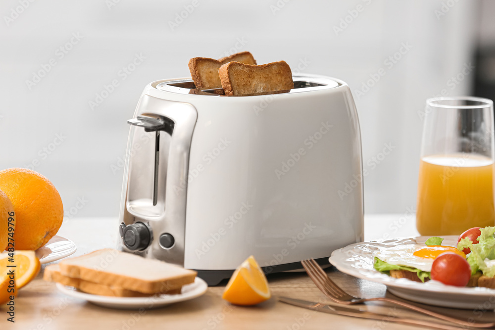 White toaster with tasty breakfast on table in light kitchen