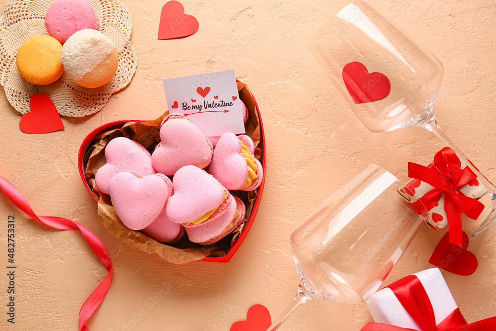 Box with tasty heart-shaped macaroons, greeting card, glasses and gifts on beige background