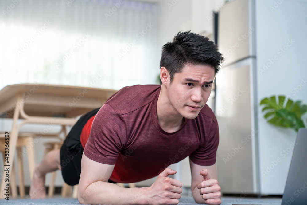 Asian handsome active young man doing push up on floor in living room.