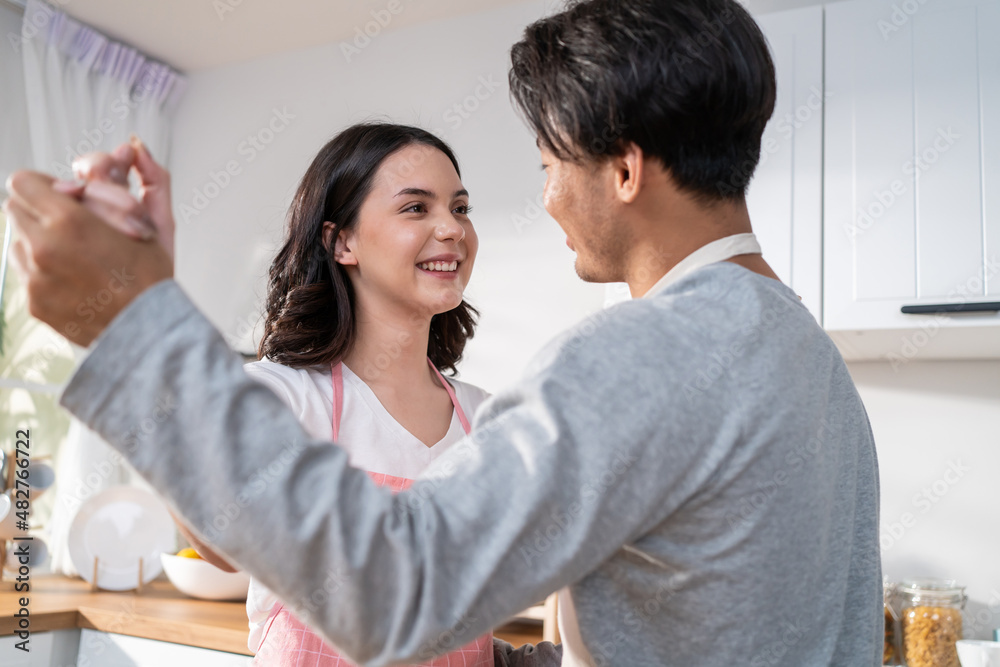 Asian attractive loving couple enjoy dance together in kitchen at home