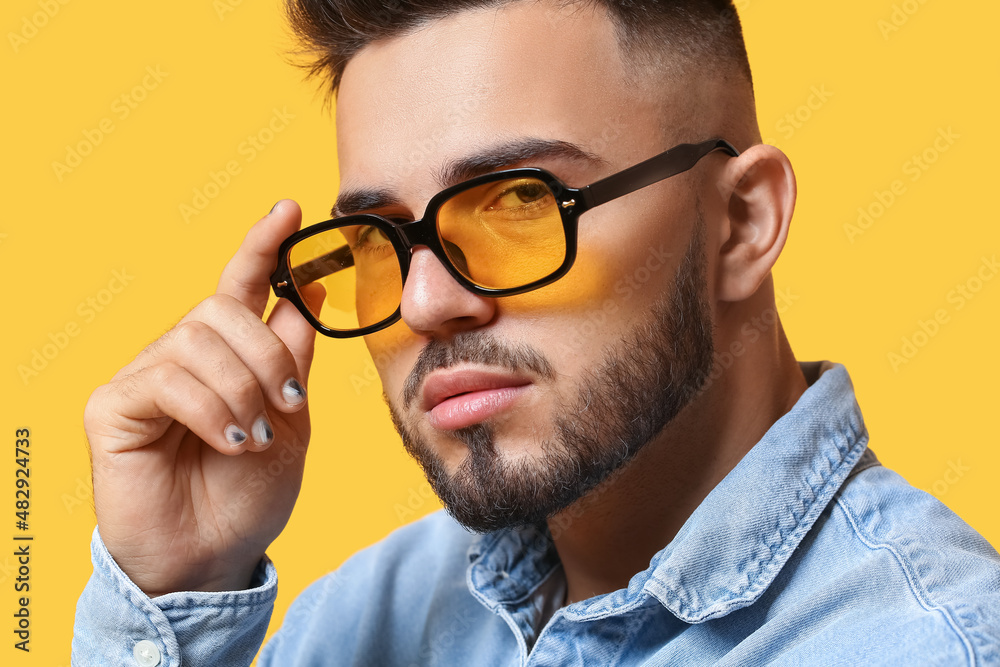 Portrait of young man with stylish manicure wearing sunglasses on color background