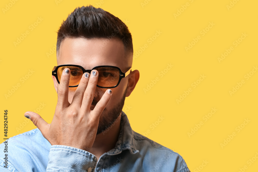 Young man with stylish manicure adjusting sunglasses on color background