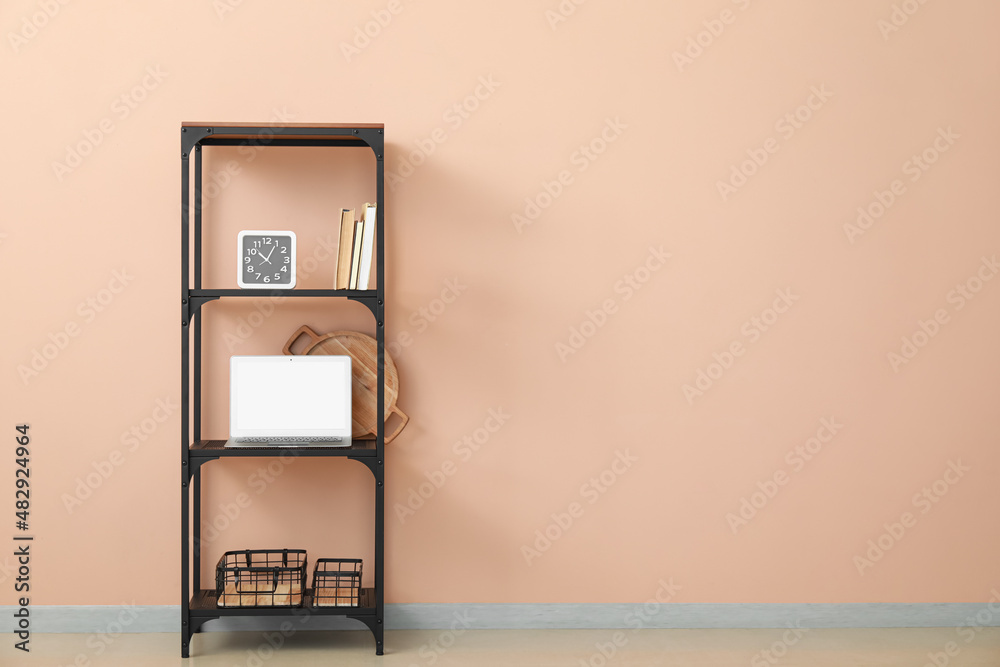 Stylish shelf unit with decor and modern laptop near color wall in room