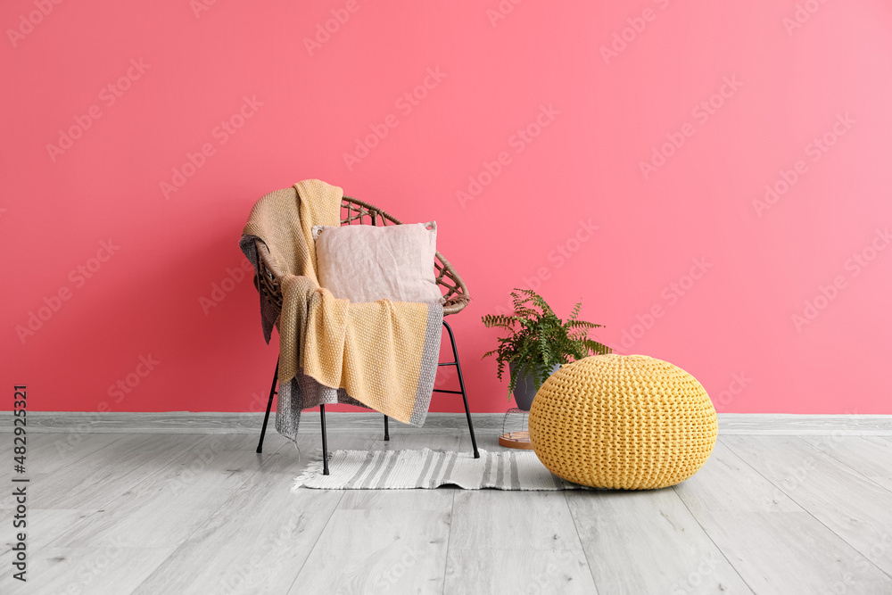 Pouf, houseplant, armchair with plaid and pillow near color wall in room