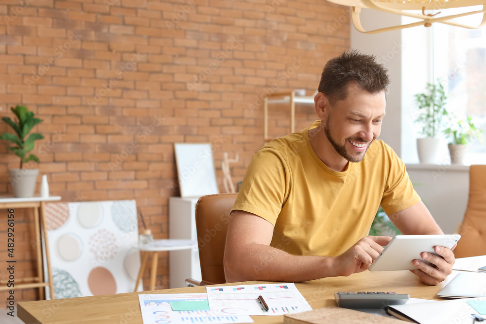 Handsome man working with tablet computer at table in office