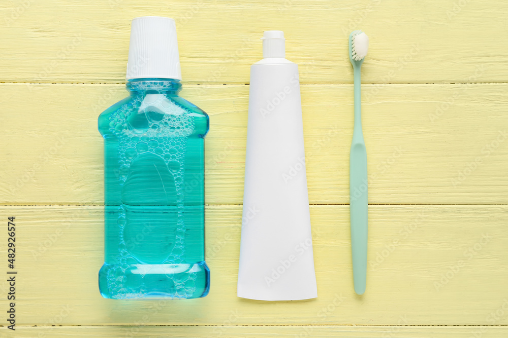 Tube with tooth paste, brush and mouthwash on color wooden background