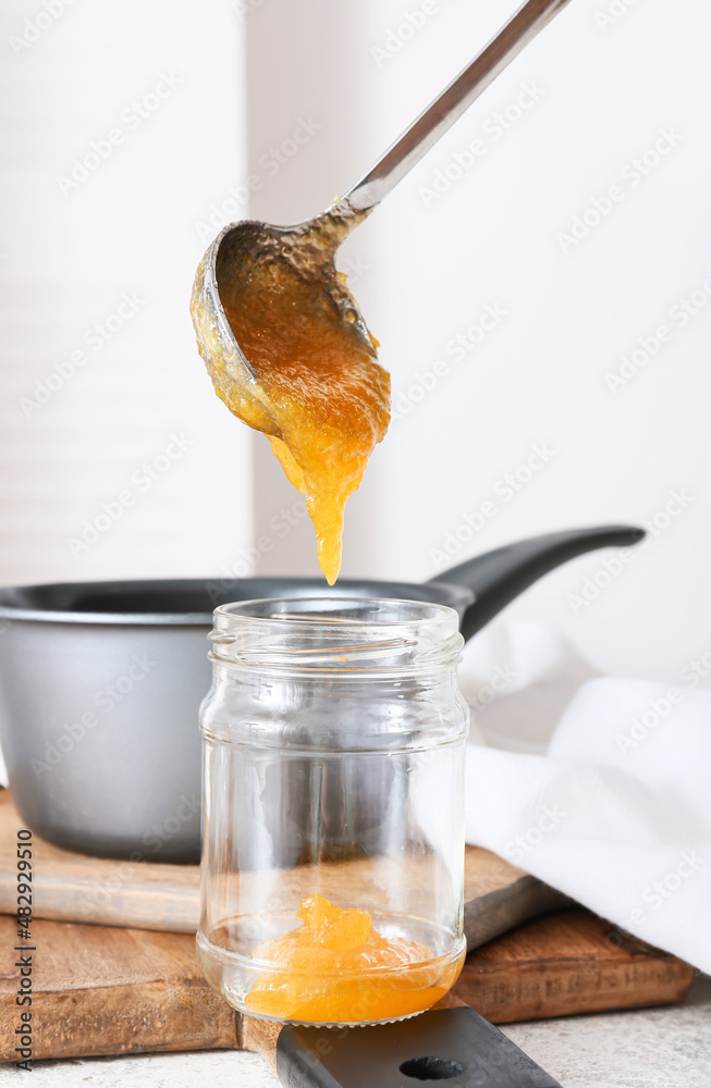 Woman pouring tasty kumquat jam into jar at kitchen table