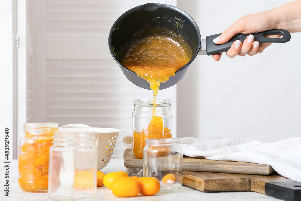 Woman pouring tasty kumquat jam into jar at kitchen table