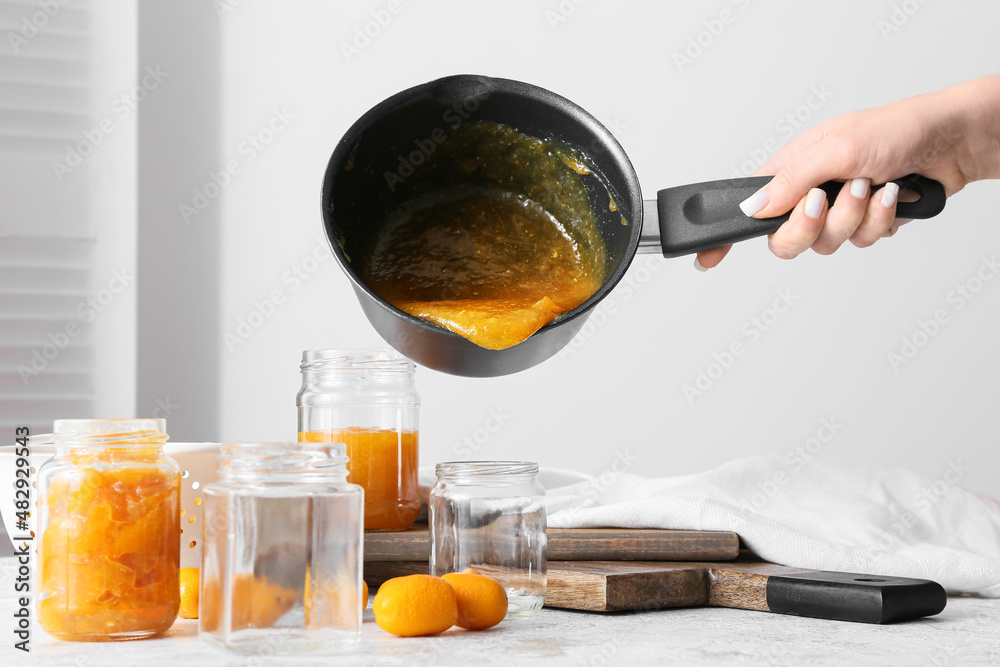 Woman pouring tasty kumquat jam into jar at kitchen table