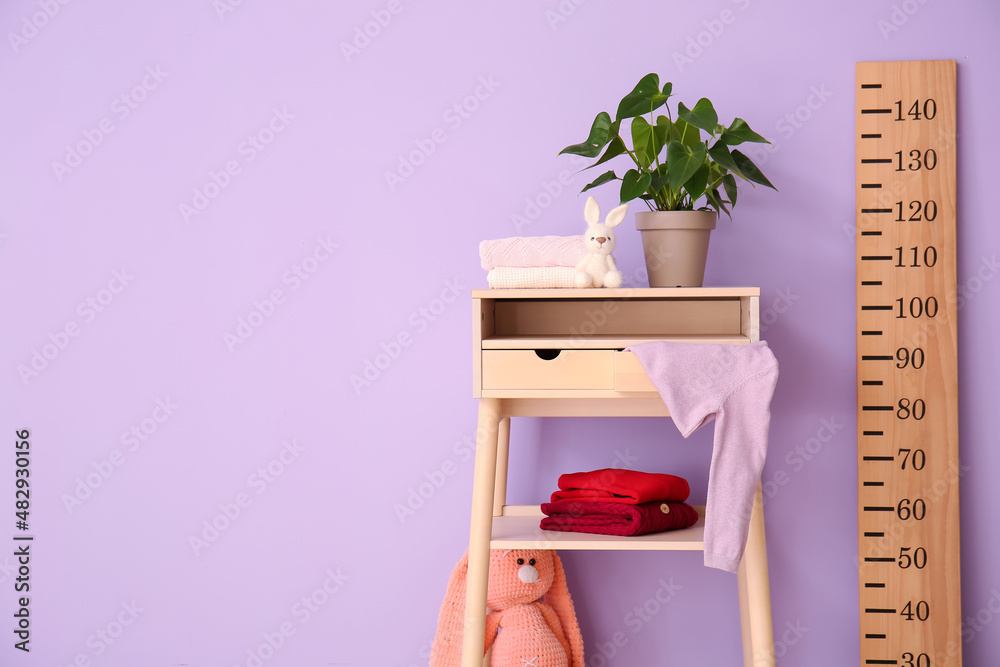 Houseplant, sweaters on standing desk and big wooden ruler near color wall