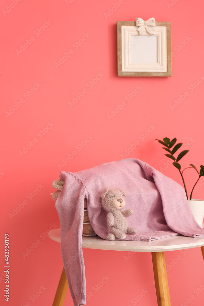 Childrens sweater, houseplant on table and blank photo frame on color wall