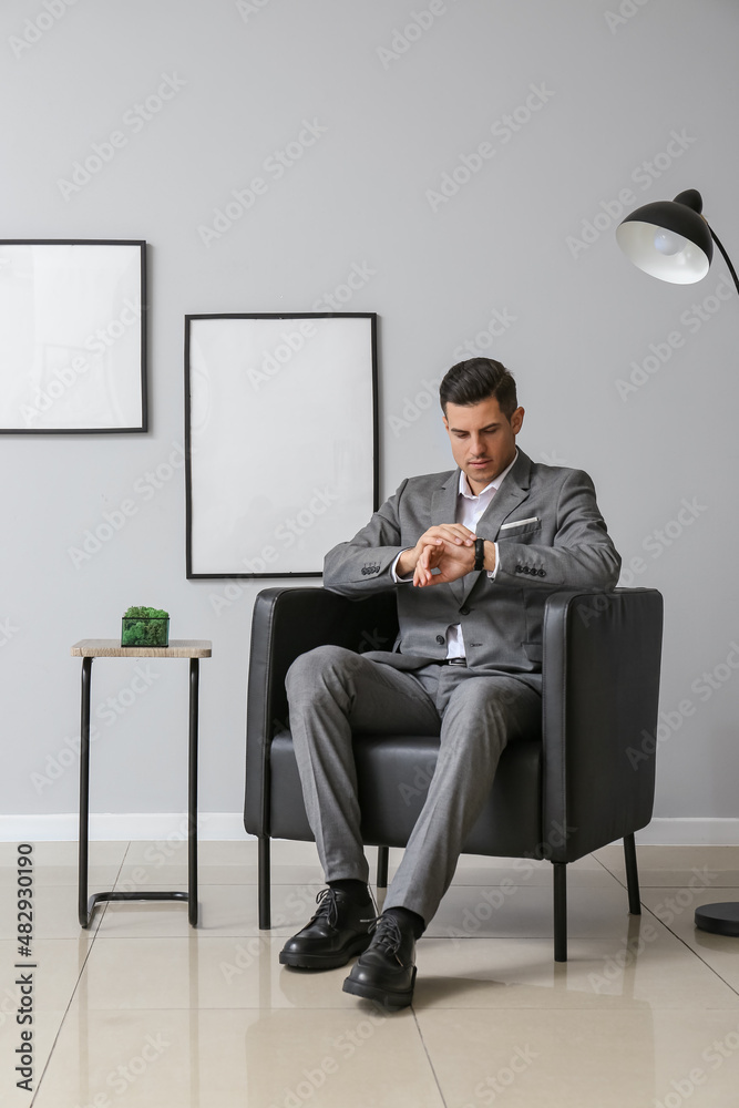 Handsome man in elegant suit sitting in armchair and checking watch