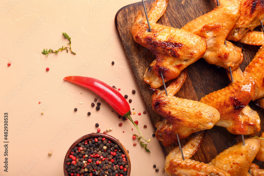 Wooden board with grilled chicken wings skewers on beige background