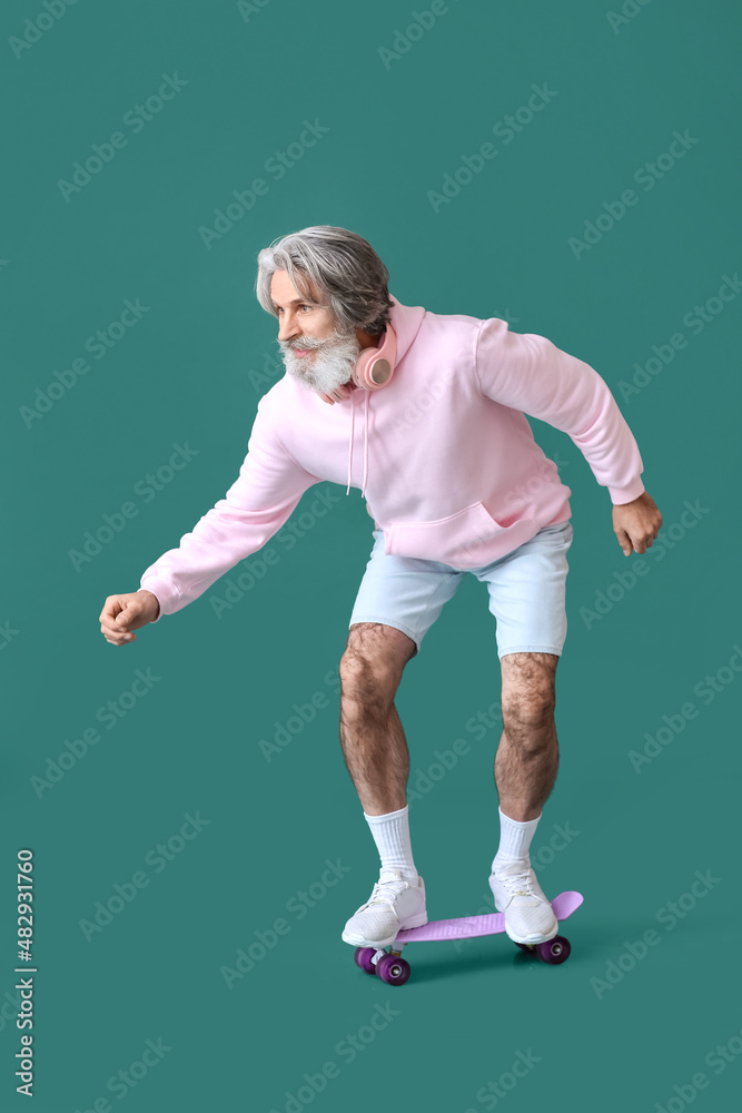 Senior man with skateboard on green background