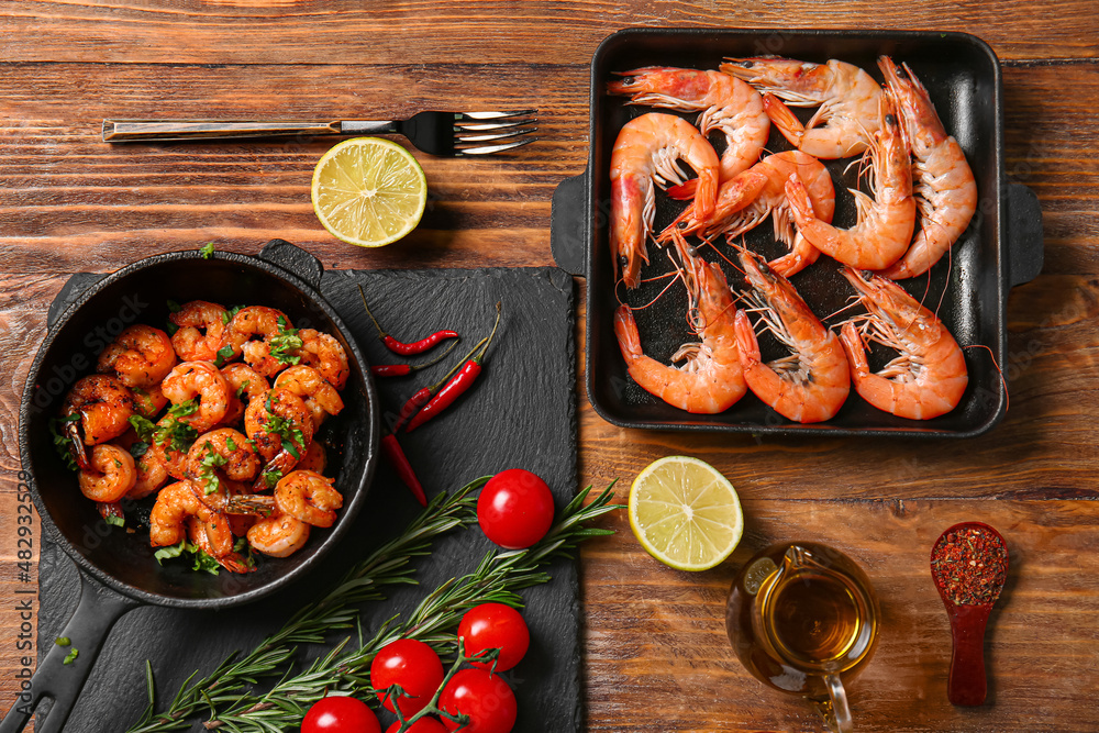 Baking dish and frying pan of tasty shrimps with lemon on wooden background