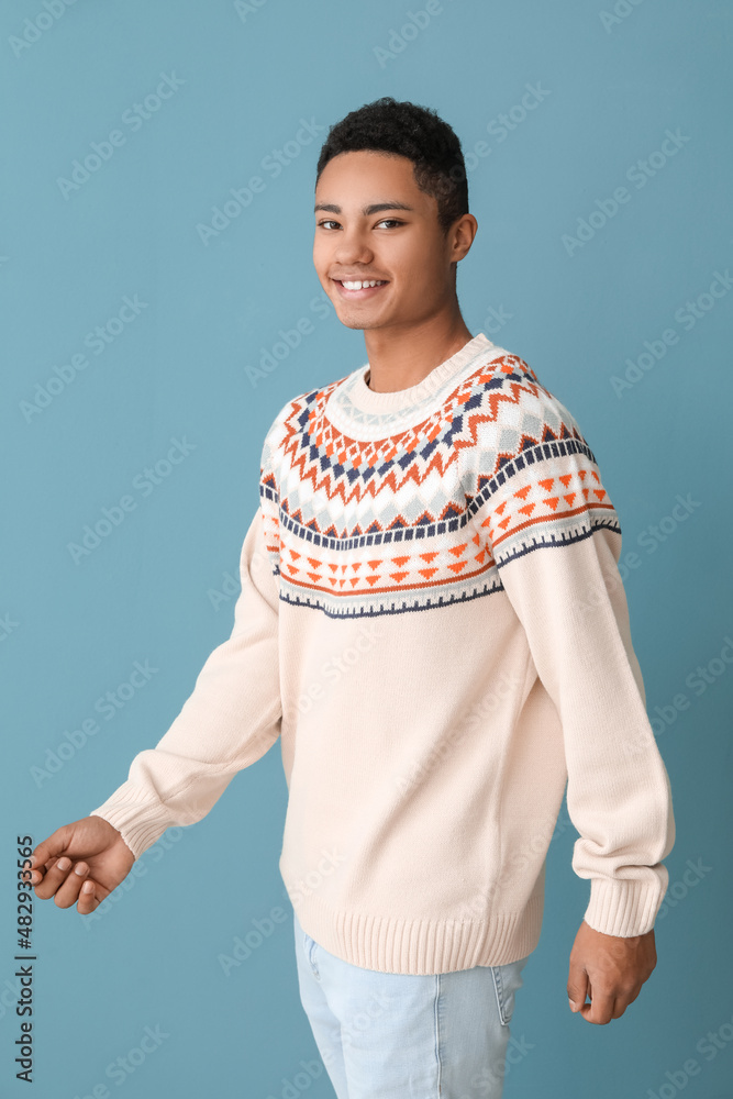 Handsome African-American guy in knitted sweater on color background