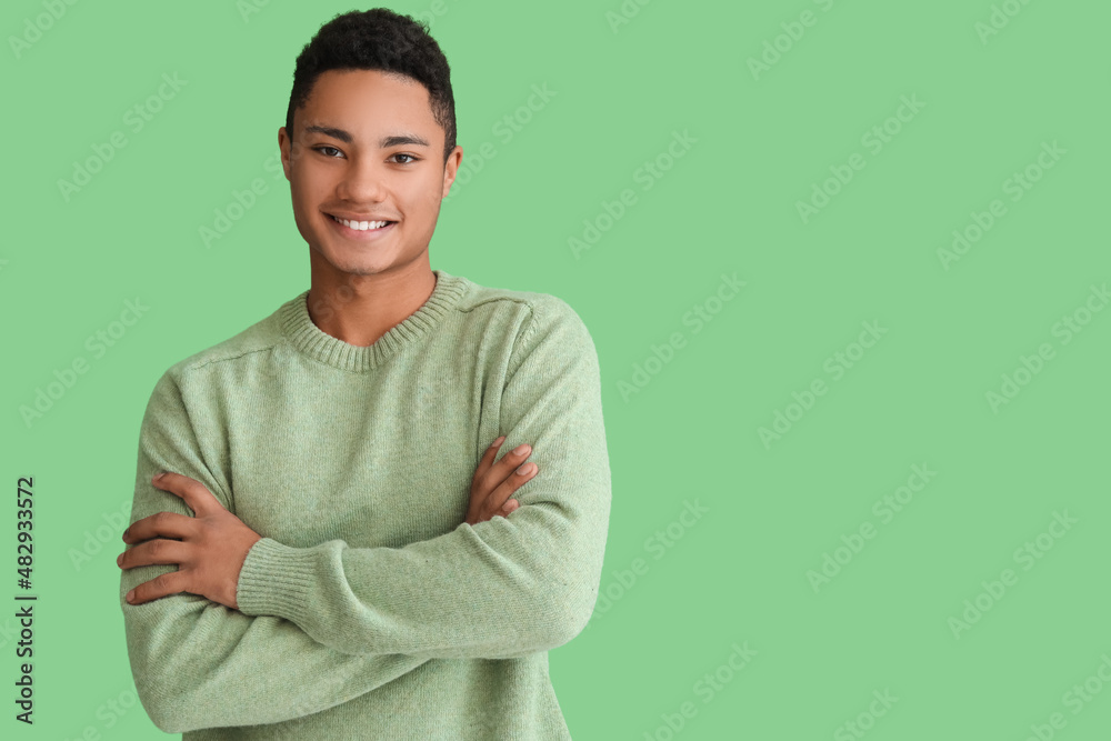 Handsome African-American guy in knitted sweater on color background