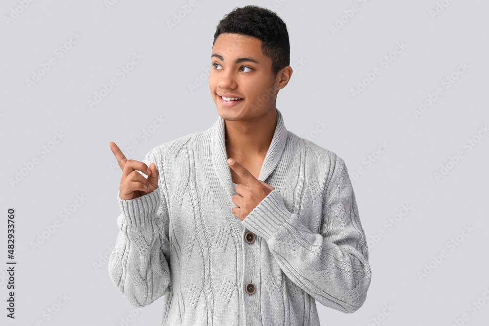 Handsome African-American guy in knitted sweater pointing at something on light background