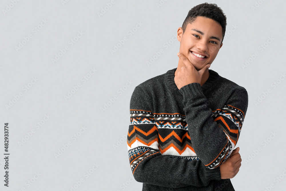 Handsome African-American guy in knitted sweater on light background