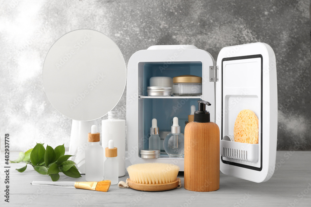 Small refrigerator with cosmetic products on light wooden table