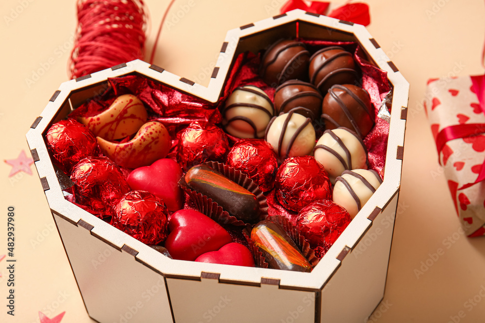 Heart shaped box with tasty chocolate candies on beige background, closeup