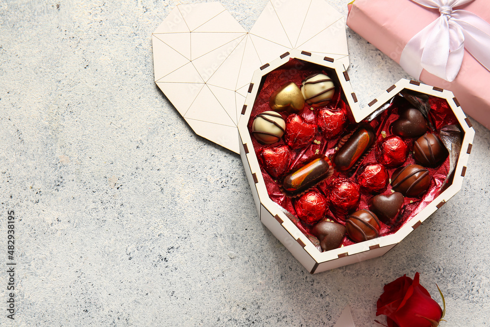 Heart shaped box with tasty chocolate candies on light background