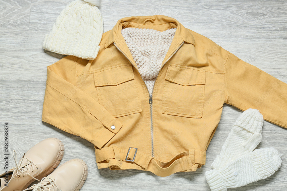 Female jacket, knitted hat, mittens and shoes on grey wooden background