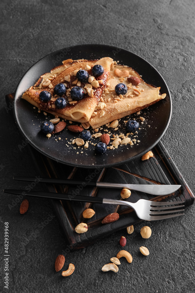 Plate of tasty thin pancakes with chocolate paste, blueberries and nuts on black background