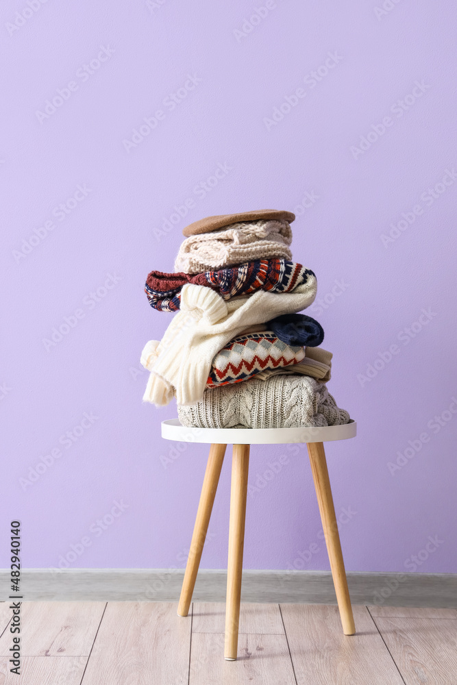 Stack of winter sweaters on table near lilac wall