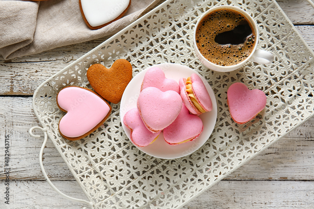 Tray with tasty heart-shaped macaroons and cup of coffee on white wooden background