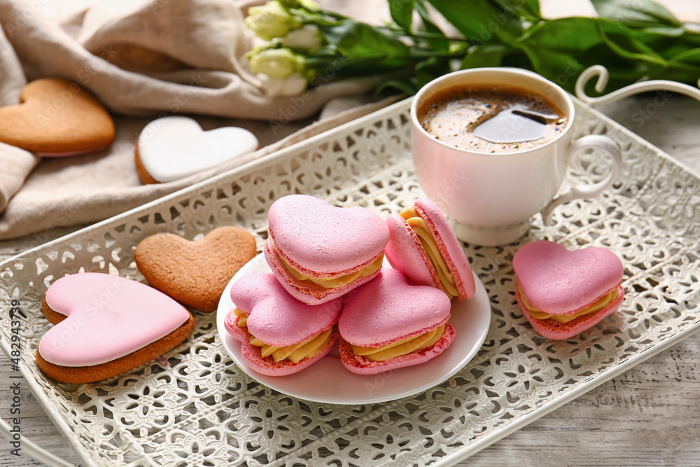 Tray with tasty heart-shaped macaroons and cup of coffee on table