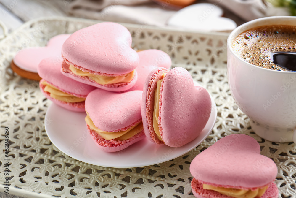 Tray with tasty heart-shaped macaroons and cup of coffee on table