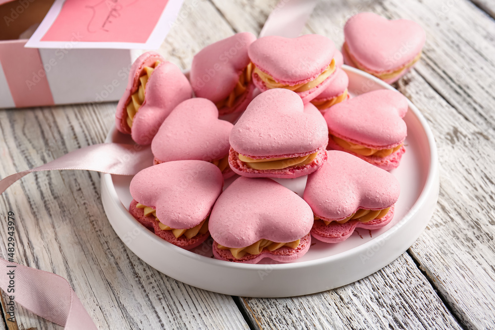 Plate with tasty heart-shaped macaroons on white wooden background