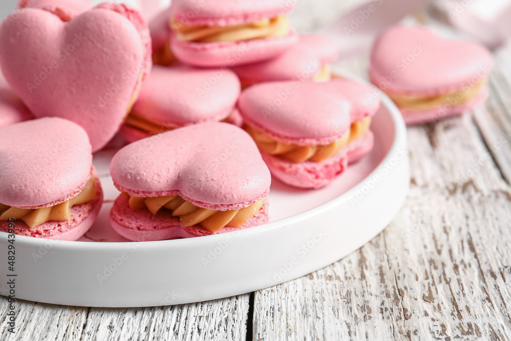 Plate with tasty heart-shaped macaroons on white wooden background, closeup