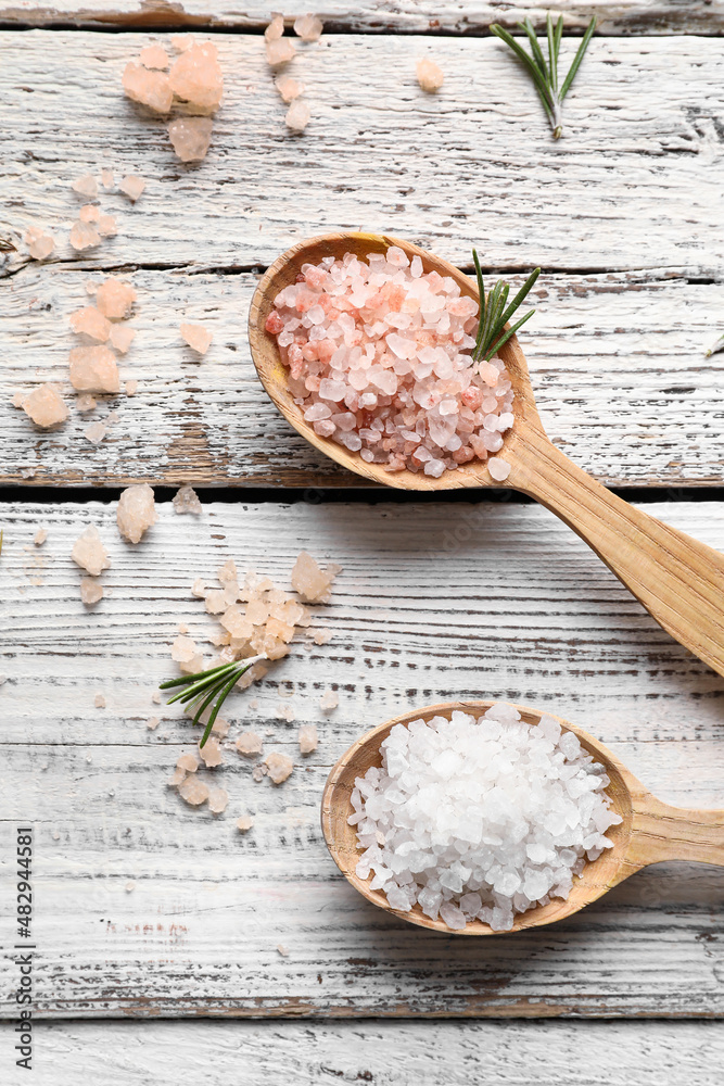 Spoons with sea salt on light wooden background, closeup