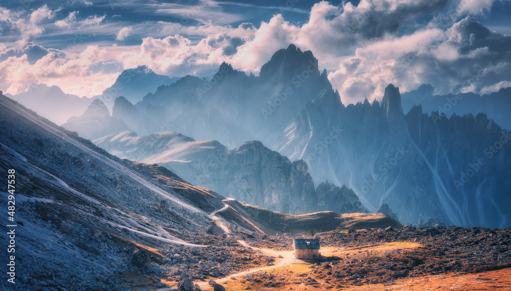 Small house in beautiful mountain valley, orange grass, stones, blue sky with clouds at sunset in su