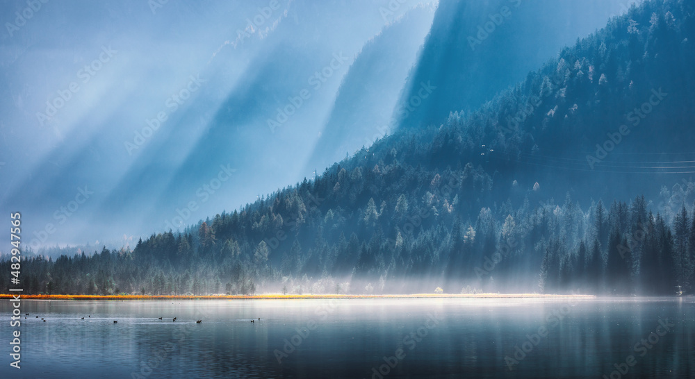 Mountains in bright sunbeams and foggy lake at sunny morning in summer. Dolomites, Italy. Landscape 